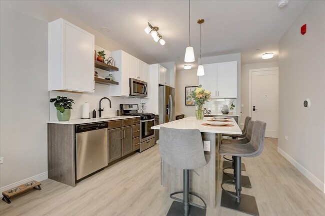 Kitchen with island, stainless steel whirlpool appliances, quartz countertops, floating shelves and two tone cabinets - Lilac Station Apartments