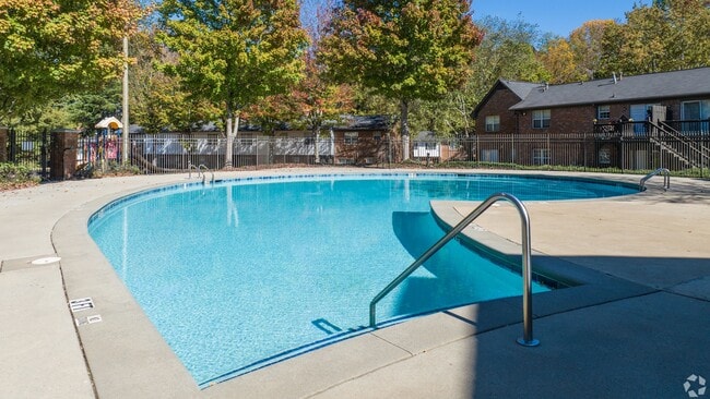 Dive into relaxation at our sparkling pool area featuring an expansive sundeck surrounded by lush trees and comfortable seating.