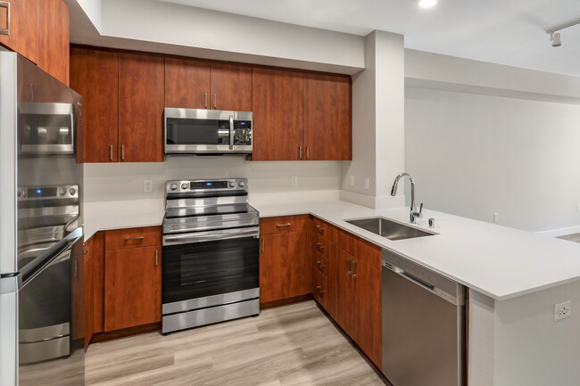 Renovated Package I kitchen with stainless steel appliances, white quartz countertops, cherry cabinetry, and hard surface flooring