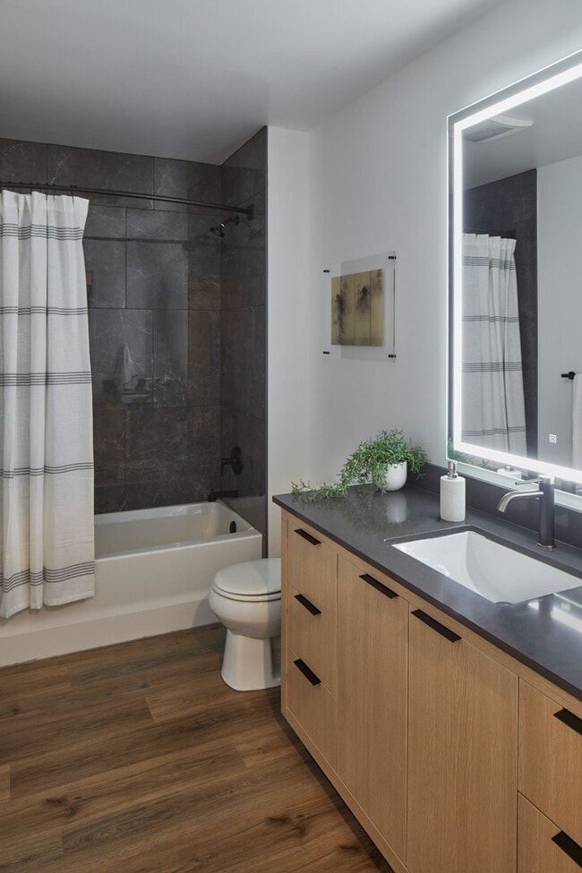 Apartment bathroom with wood-style flooring and LED vanity mirror. - Griffis Seattle Waterfront