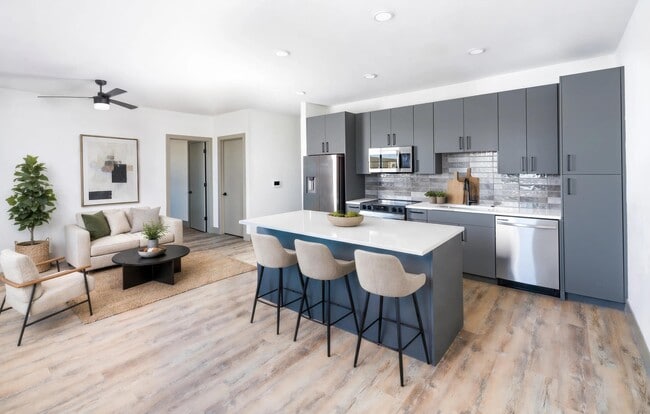 Open-concept kitchen and living area with a large island, stainless steel appliances, design-forward tile backsplash, and wood-style flooring throughout.
