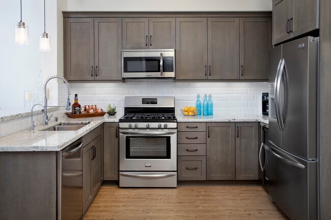 Kitchens with grey cabinetry, grey speckled granite countertops, white subway tile backsplash, stainless steel appliances, and hard surface flooring