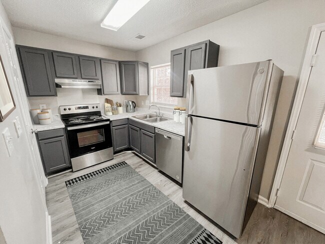 Kitchen with stainless steel appliances, gray cabinets, decorative accents, patterned rug, and marble style countertops