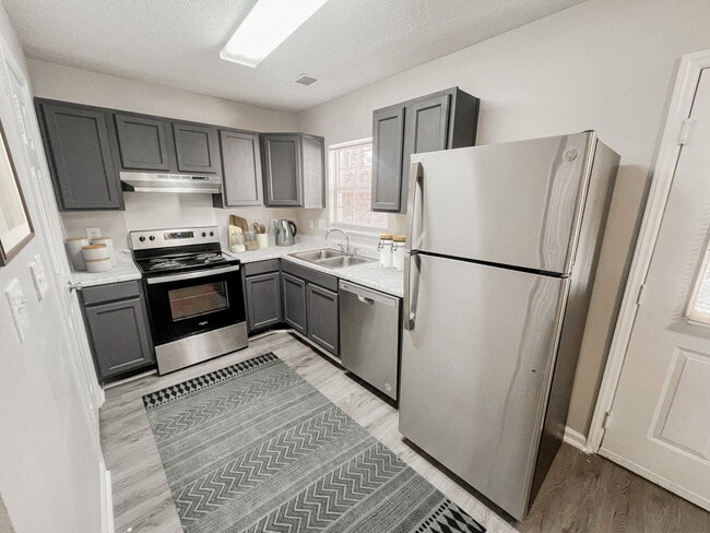 Kitchen with stainless steel appliances, gray cabinets, decorative accents, patterned rug, and marble style countertops - Pendleton Townhomes