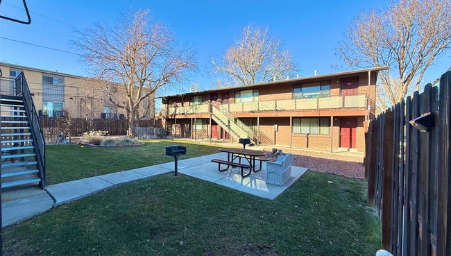 Cozy apartment complex with charming red doors and an inviting courtyard featuring a picnic area and barbecue spot, surrounded by lush greenery.