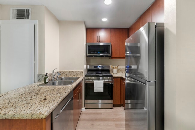 Renovated Package I kitchen with stainless steel appliances, beige speckled granite countertops, chestnut cabinetry, and hard surface flooring