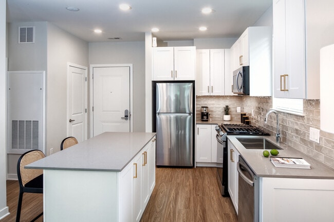 Design Collection II (South Building) Kitchen with white cabinetry, gold pulls, beige tile backsplash, grey quartz countertops, stainless steel appliances, and hard surface flooring