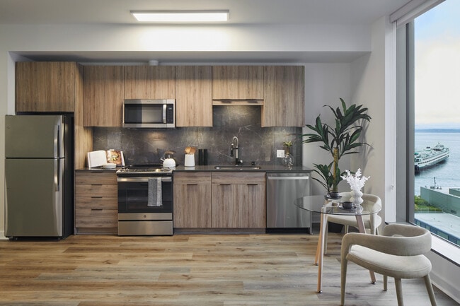 Apartment kitchen with stainless steel appliances, quartz countertops and wood-style flooring. - Griffis Seattle Waterfront Apartments