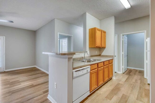 Kitchen view showing breakfast bar, wood cabinets, dishwasher, laminate countertops, and open connection to living area