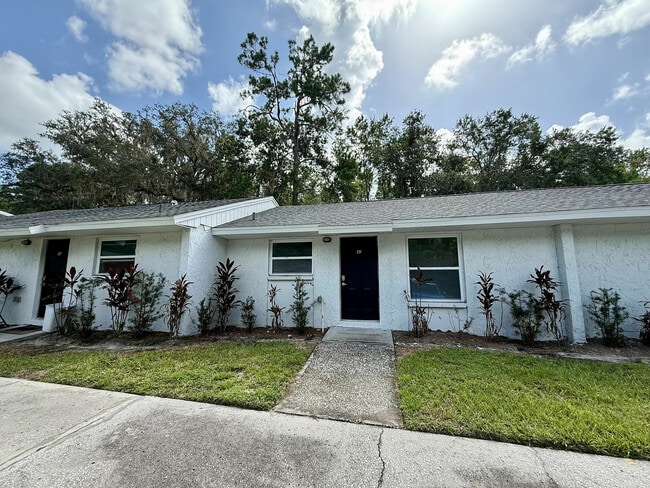 Charming single-story apartment with fresh white exterior, modern black doors, and lush landscaping under a clear blue sky. - Sunny Creek Apartments