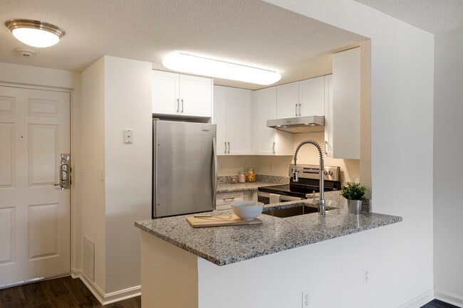 Renovated Package III kitchen with white cabinetry, grey granite countertops, stainless steel appliances, and hard surface flooring - eaves Washingtonian Center Apartments