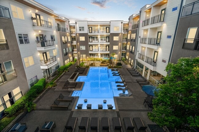Zona de piscina estilo resort con plataforma para tomar el sol, tumbonas y chimenea exterior. - Larq Henderson