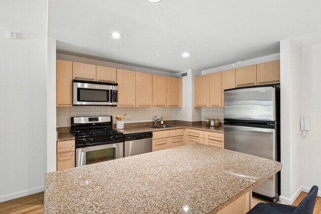 Classic Package I kitchen with beige speckled countertops, beige cabinets, stainless steel appliances, and hard surface flooring