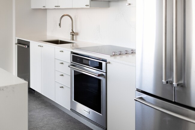 Signature Collection kitchen with white cabinetry, white marbled quartz countertop and backsplash, wine fridge, and upgraded stainless steel appliances - Avalon South Miami