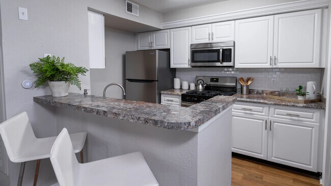 Prepare comidas con facilidad en esta elegante cocina, completa con electrodomésticos de acero inoxidable, gabinetes blancos y una barra de desayuno perfecta para cenas informales. - The Enclave at Huntington Woods