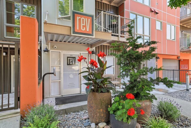 Street-level entrance to REV Fremont featuring secure access, colorful modern facade accents, and landscaped planters.