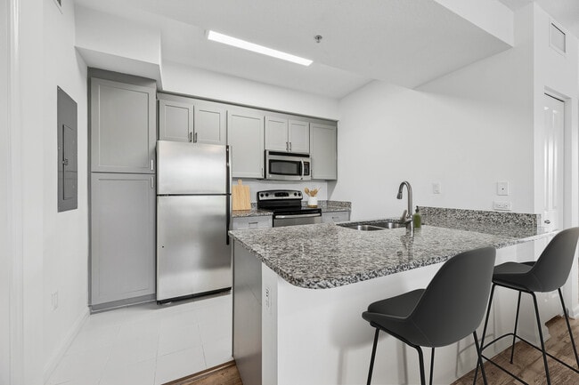 Renovated Package I kitchen with stainless steel appliances, tile backsplash, granite countertops (in most homes), and grey cabinetry