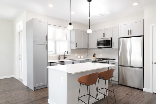 Modern kitchen with stainless steel appliances, white quartz countertop, light grey cabinetry, white tile backsplash, and hard surface flooring - Avalon Amityville Apartments