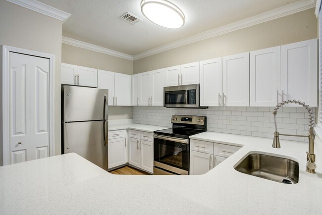 Image of a kitchen with wrap around quartz counters and a ceramic backsplash. - Amara at Metro West Apartments