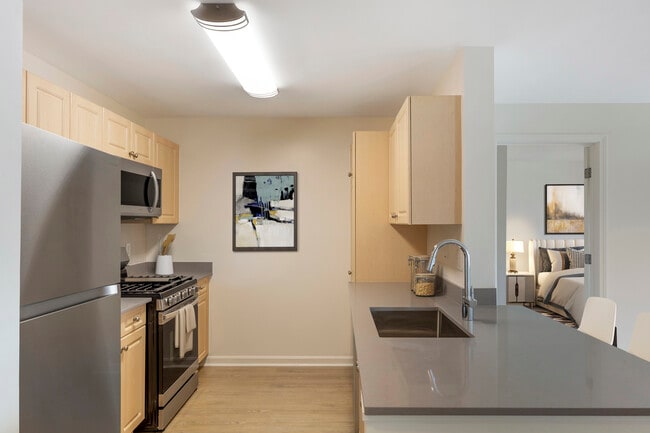 Phase I Renovated Package I apartment kitchen with stainless steel appliances, grey quartz countertops, oak cabinetry, and hard surface flooring