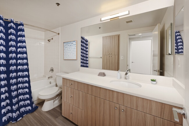 Baño renovado del Paquete II con encimeras de cuarzo blanco, gabinetes de madera y pisos de superficie dura
