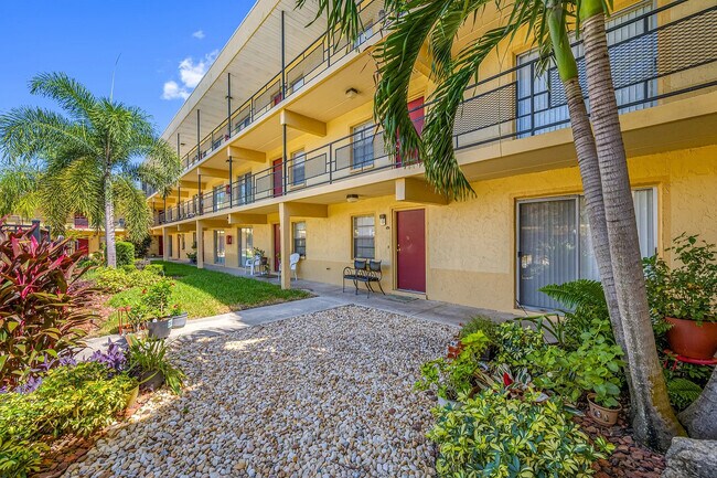 Charming two-story apartment community with vibrant garden landscaping and palm trees, set under a clear blue sky.