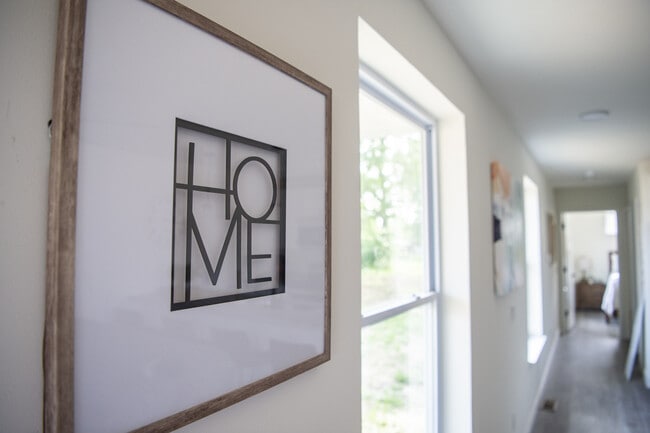 Hall de entrada acogedor con grandes ventanales, luz natural y una elegante pieza de arte 'HOME' que conduce a una habitación acogedora.