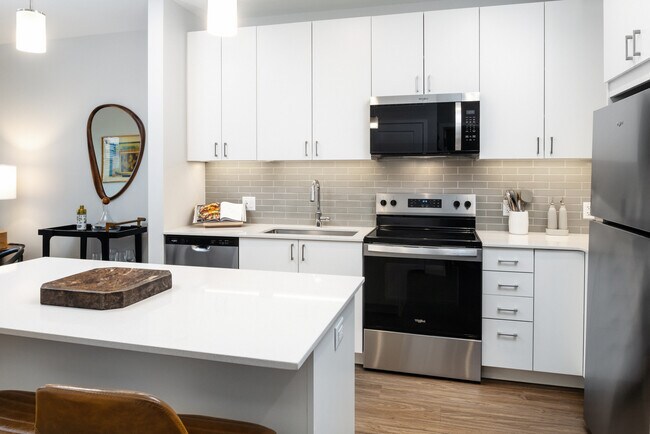 Design Collection I kitchen with stainless steel appliances, white cabinetry, grey tile backsplash, under-cabinet lighting, white quartz countertops, and hard surface flooring