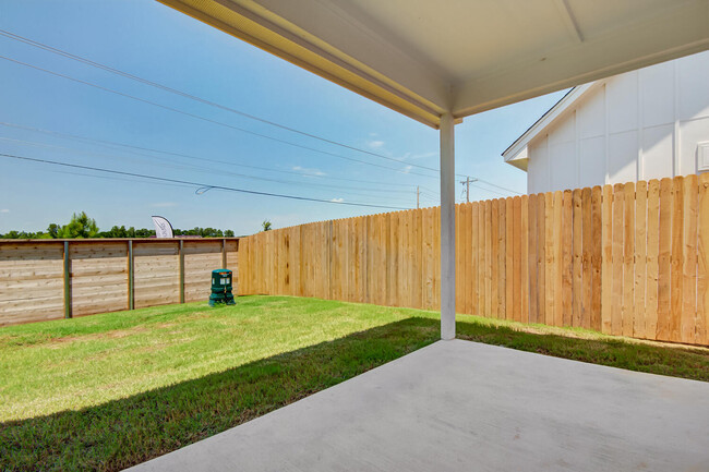 Covered backyard patio with concrete slab, wooden privacy fence and grassy yard - Legacy Farms