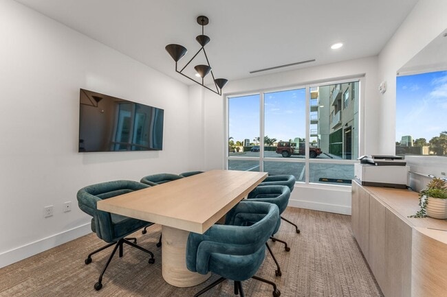 Modern conference room with a sleek wooden table, six plush teal chairs, and a large window offering a bright, spacious atmosphere. - Triton Cay - Daytona Apartments