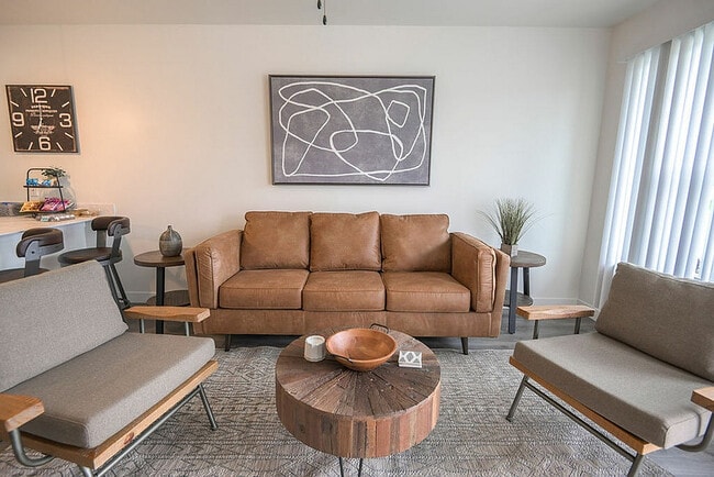 Elegante sala de estar con un elegante sofá de cuero marrón, obras de arte modernas y una mesa de café de madera rústica, que crean un ambiente acogedor y elegante.