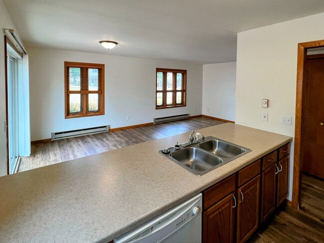 bright kitchen with ample countertop space, wood cabinetry, and dishwasher overlooking living area