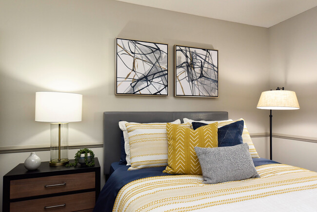 Relax in this elegantly designed bedroom, where comfort meets style with abstract art and plush bedding. - Everly at Meridian Hills Apartments