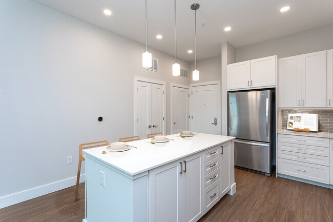 Modern kitchen with white cabinetry, undercabinet lighting, grey tile backsplash, and white quartz countertops - Avalon Carmel Commons