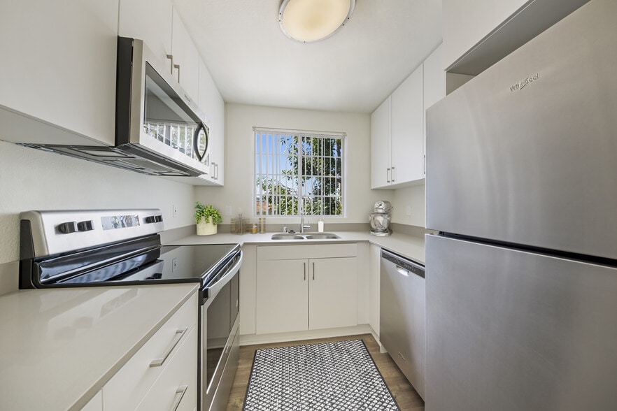Renovated Package kitchen with white cabinetry, grey quartz countertops, stainless steel appliances, upgraded lighting and fixtures, and hard surface flooring throughout kitchen, dining area, and bath.
