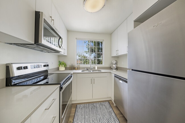 Upgraded Package kitchen with white cabinetry, grey quartz countertops, stainless steel appliances, upgraded lighting and fixtures, and hard surface flooring throughout - eaves La Mesa Apartments