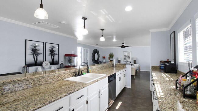 Spacious and modern kitchen with granite countertops, stylish pendant lighting, and open floor plan leading to a cozy living area. - Advenir at The Meadows