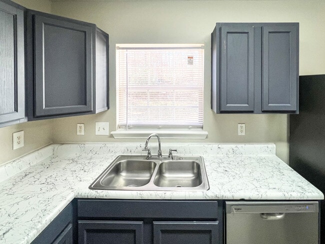 Kitchen sink area with double basin stainless sink, marble style counters, window with blinds, and dark upper cabinets