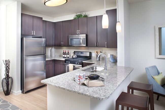 Classic Package kitchen with stainless steel appliances, white speckled granite countertops, espresso cabinetry, beige tile backsplash, and hard surface flooring