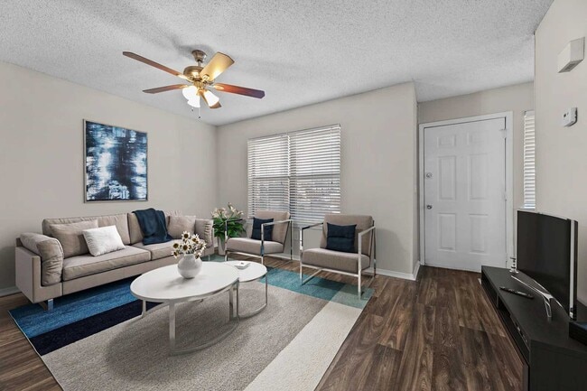Living room with beige sofa, white oval coffee table, blue accent chairs, patterned rug, ceiling fan, and wood-look floors