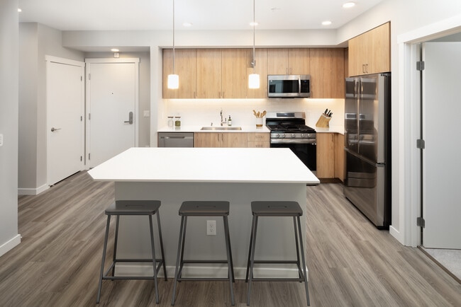 Kitchen with white quartz countertops, oak cabinetry, white subway tile backsplash, stainless steel appliances, and hard surface flooring