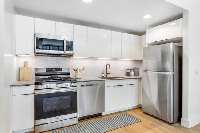 Renovated Package I kitchen with grey quartz countertops, white cabinetry, light grey tile backsplash, stainless steel appliances, and hard surface flooring - Avalon Morningside Park