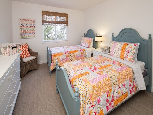 Bedroom with carpet floors, a white dresser, ceiling fan, and two full sized beds with colorful bedding.
