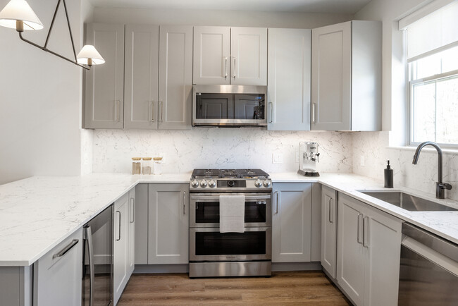 Signature Collection kitchen with stainless steel appliances, white quartz countertop, grey cabinetry, white quartz backsplash, and hard surface flooring - Avalon Princeton Circle Apartments