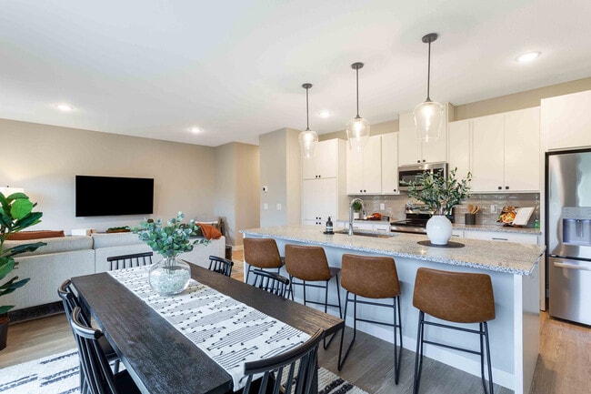 Contemporary open-plan living space featuring a stylish kitchen with modern appliances and a cozy dining area, perfect for entertaining. - Summerwell Maple Grove
