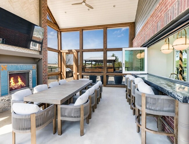 Screened-in porch with a harvest dining table, an adjacent catering kitchen and entertainment lounge inside, plus a cozy outdoor fireplace.
