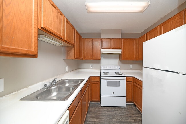 Cocina con electrodomésticos blancos, gabinetes de madera y amplio espacio en la encimera. - Prairie Creek Estates