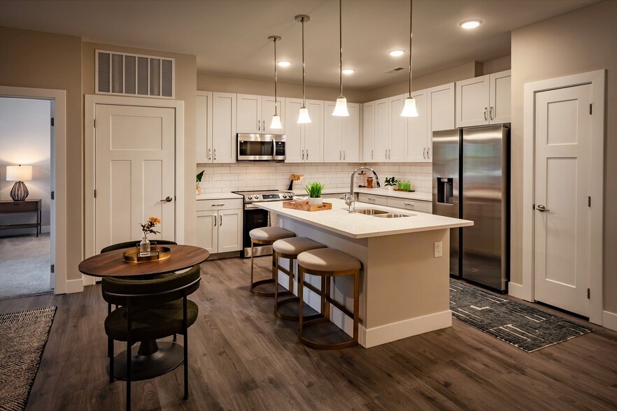 Modern apartment kitchen featuring white cabinetry, pendant lighting, stainless steel appliances, and a spacious island with bar seating for entertaining.
