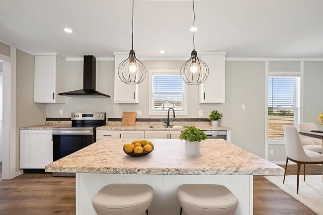 Cocina luminosa con isla de mármol, lámparas colgantes y armarios blancos que se abre a un comedor con ventanas.