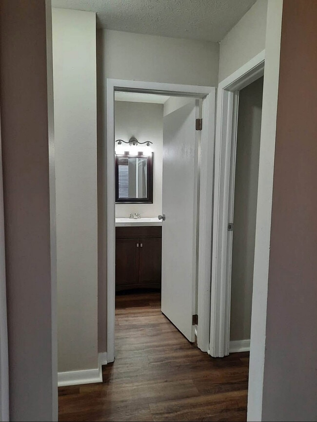 Inviting hallway with elegant hardwood flooring leading to a bright, modern bathroom with stylish fixtures.